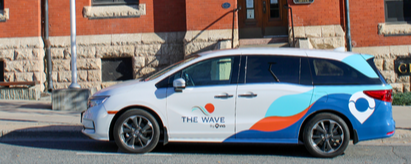 van with colourful wrap parked on street, brick building, sidewalk